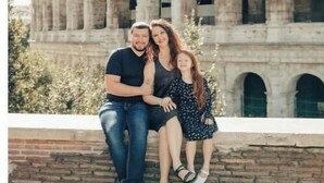 Una famiglia di tre persone seduta su un muro di mattoni di fronte al Colosseo.