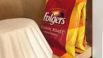 Een houten plank met een witte keramieken pot en een zak Folgers Classic Roast gemalen koffie.