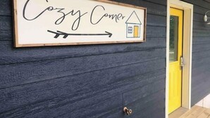 A sign on a dark wooden wall that reads "Cozy Corner" with an arrow pointing to the right.