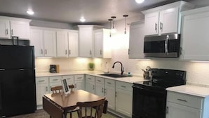 A modern kitchen with white cabinets, a black refrigerator, a microwave, and a stove. - Easy Street Apartment (Van Buren)