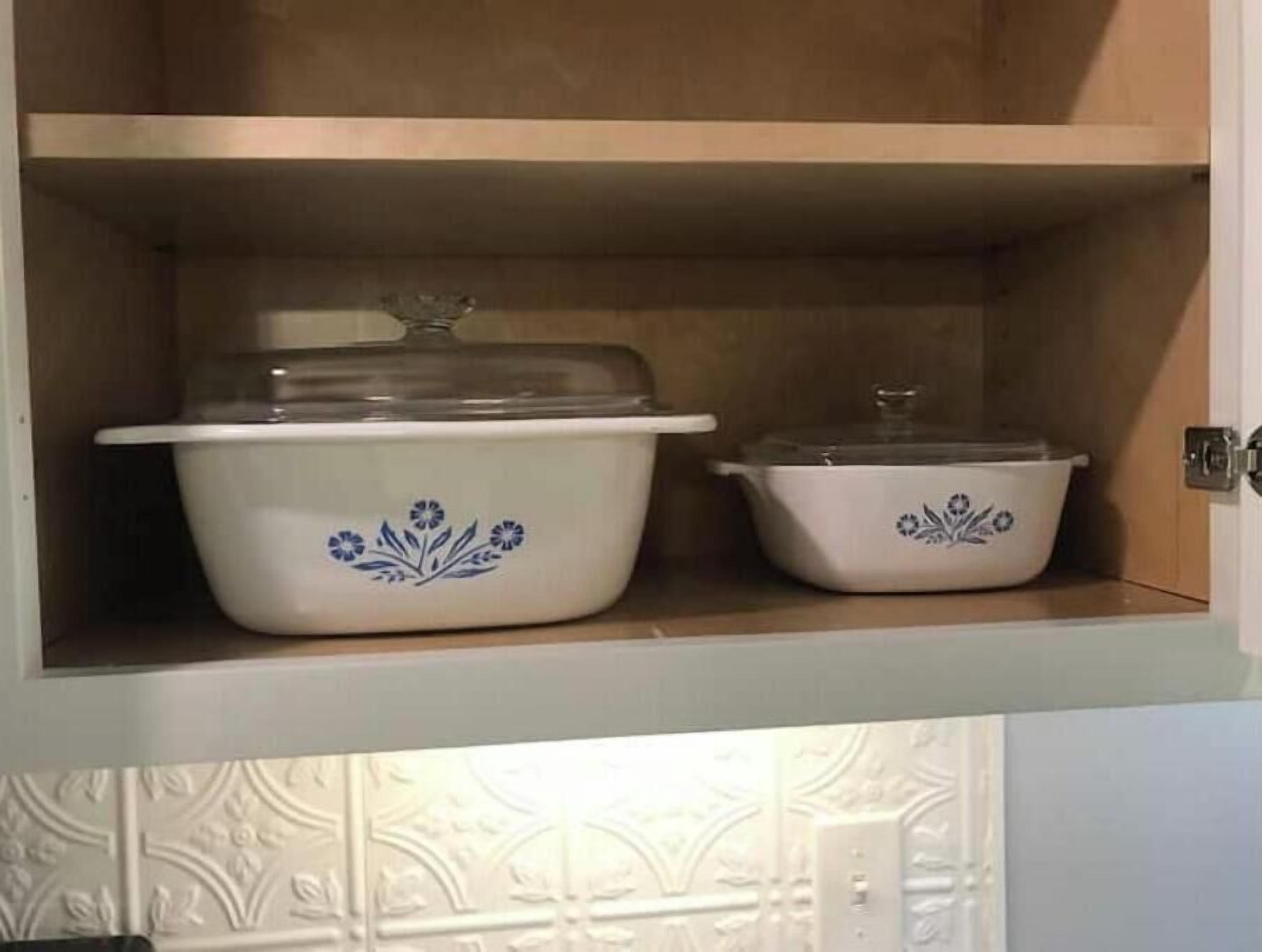 Un armario de cocina con dos ollas blancas de cerámica, cada una con tapa y diseños florales azules.