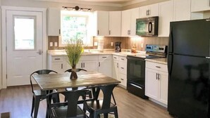 A modern kitchen with white cabinets, a black refrigerator, and a dining area with a wooden table and chairs. - River Ridge Retreat (Van Buren)