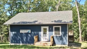A small, single-story house with a dark blue exterior, a front door, a small porch, and a sign that reads "Home Sweet Home." - River Ridge Retreat (Van Buren)