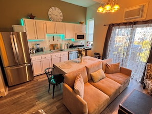 A modern kitchen with white cabinets, a stainless steel refrigerator, and a dining area with a sofa and table.