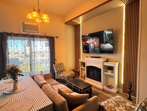 A living room with a sofa, a fireplace, a television, and a view of the city through a window.