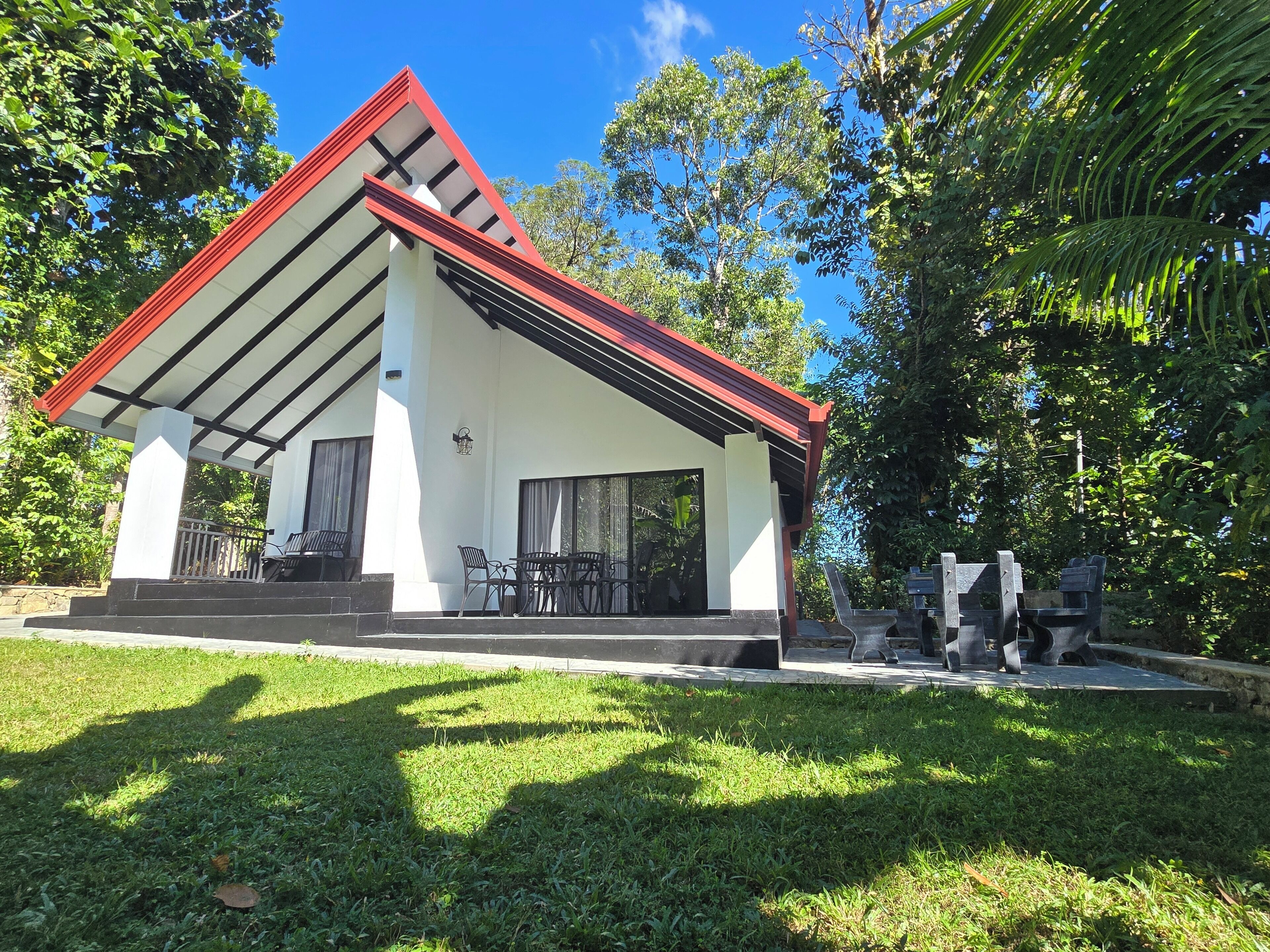 A modern building with a red roof and white walls, featuring a covered patio with outdoor furniture.