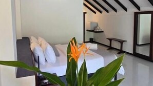 Ein modernes Zimmer mit schrägem Dach, einem Bett mit weißer Bettwäsche, einem Nachttisch und einer Pflanze in einer Vase.