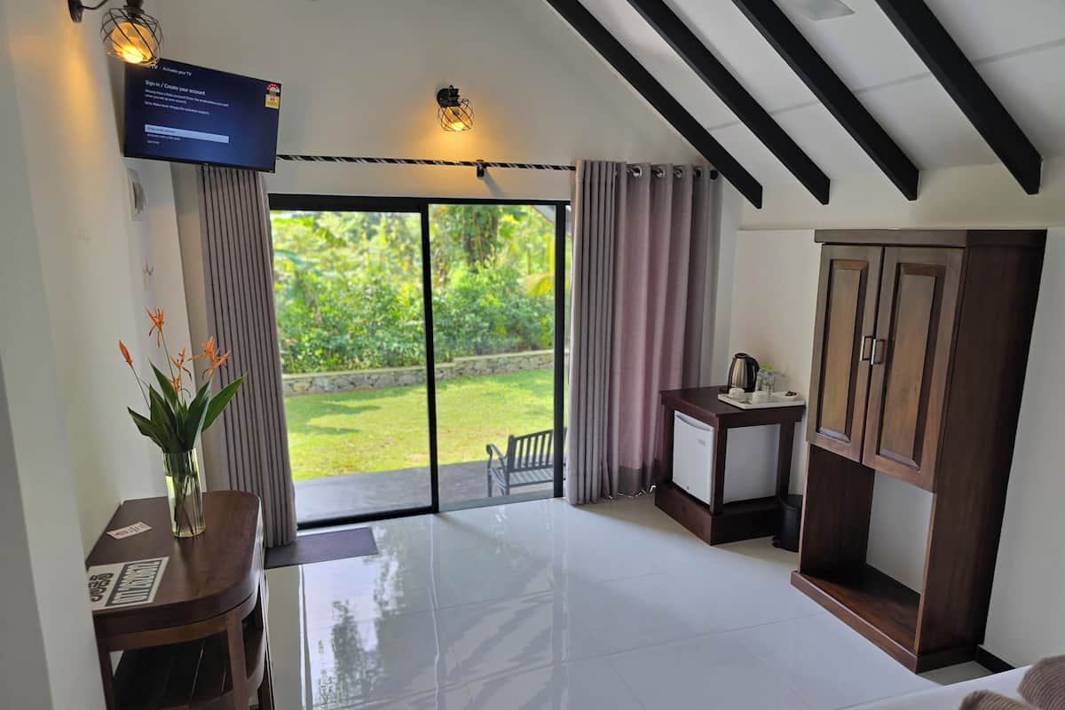 Ein Hotelzimmer mit einer großen Glasschiebetür, die zu einem Garten führt, einem kleinen Schreibtisch mit Wasserkocher und einem Bett mit weißer Daunendecke.