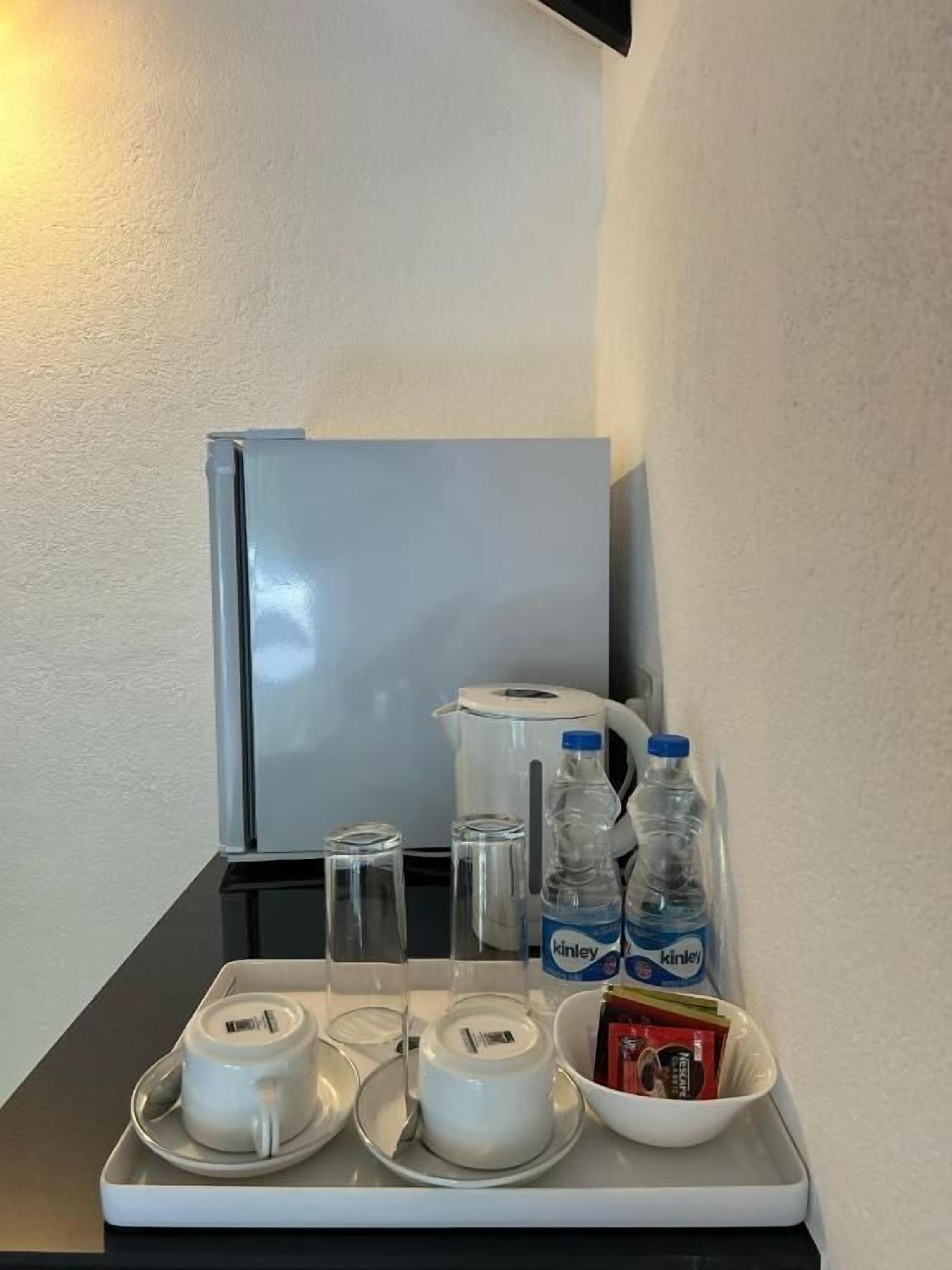 A tray with a white mug, a glass, a water bottle, a kettle, and a bowl of snacks.