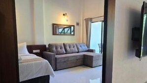 Ein modernes Hotelzimmer mit einem großen Bett, einem grauen Ecksofa, einem Deckenventilator und einem an der Wand befestigten Fernseher.