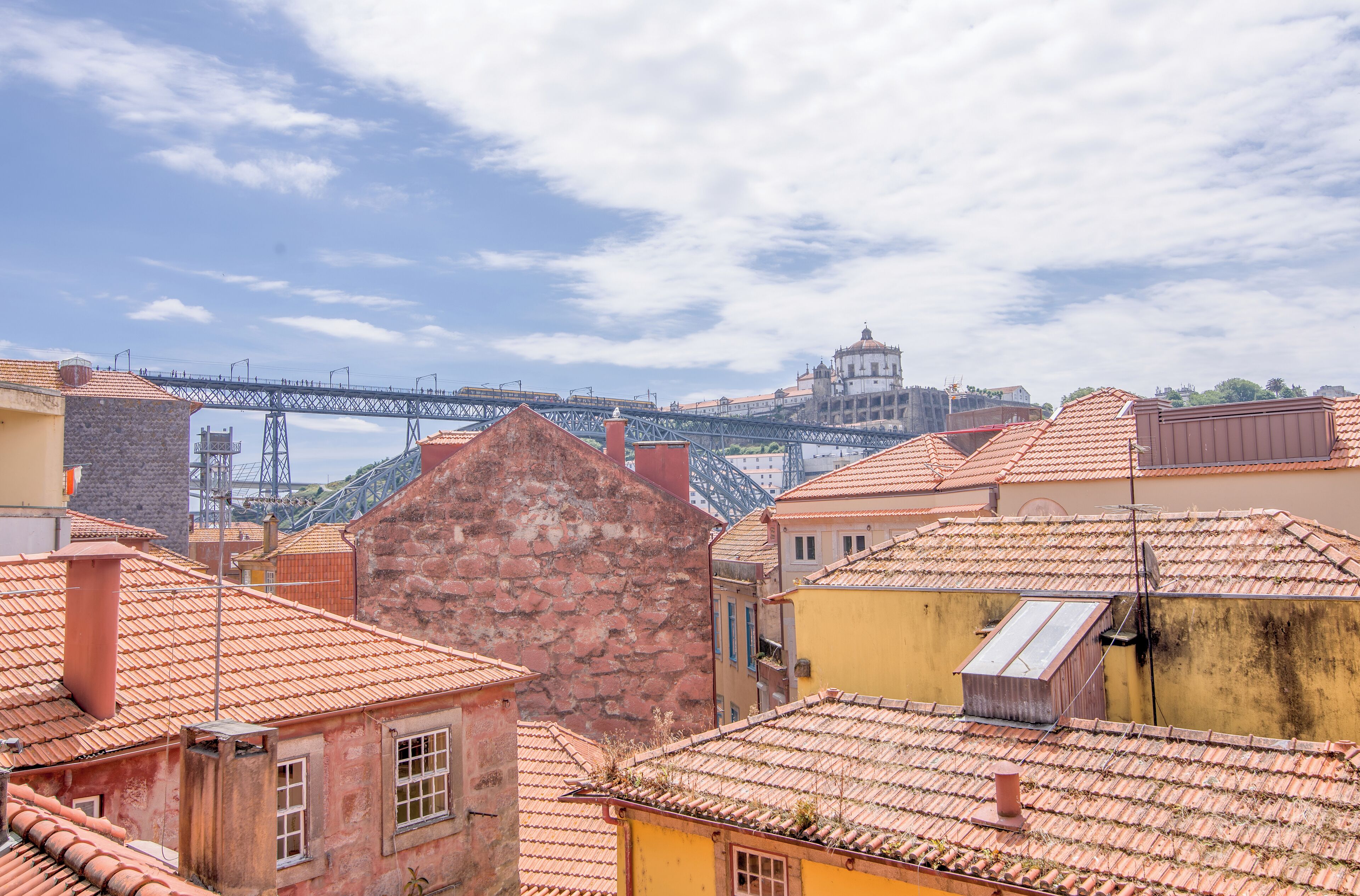 Blick auf eine Stadtlandschaft mit einer markanten Brücke im Hintergrund, historischen Gebäuden mit roten Ziegeldächern und einer Mischung aus Stein- und Backsteinfassaden.