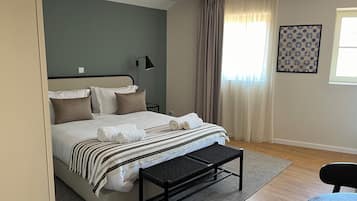 A neatly arranged bedroom with a bed, bedside table, lamp, and a view of the outdoors through a window with curtains.
