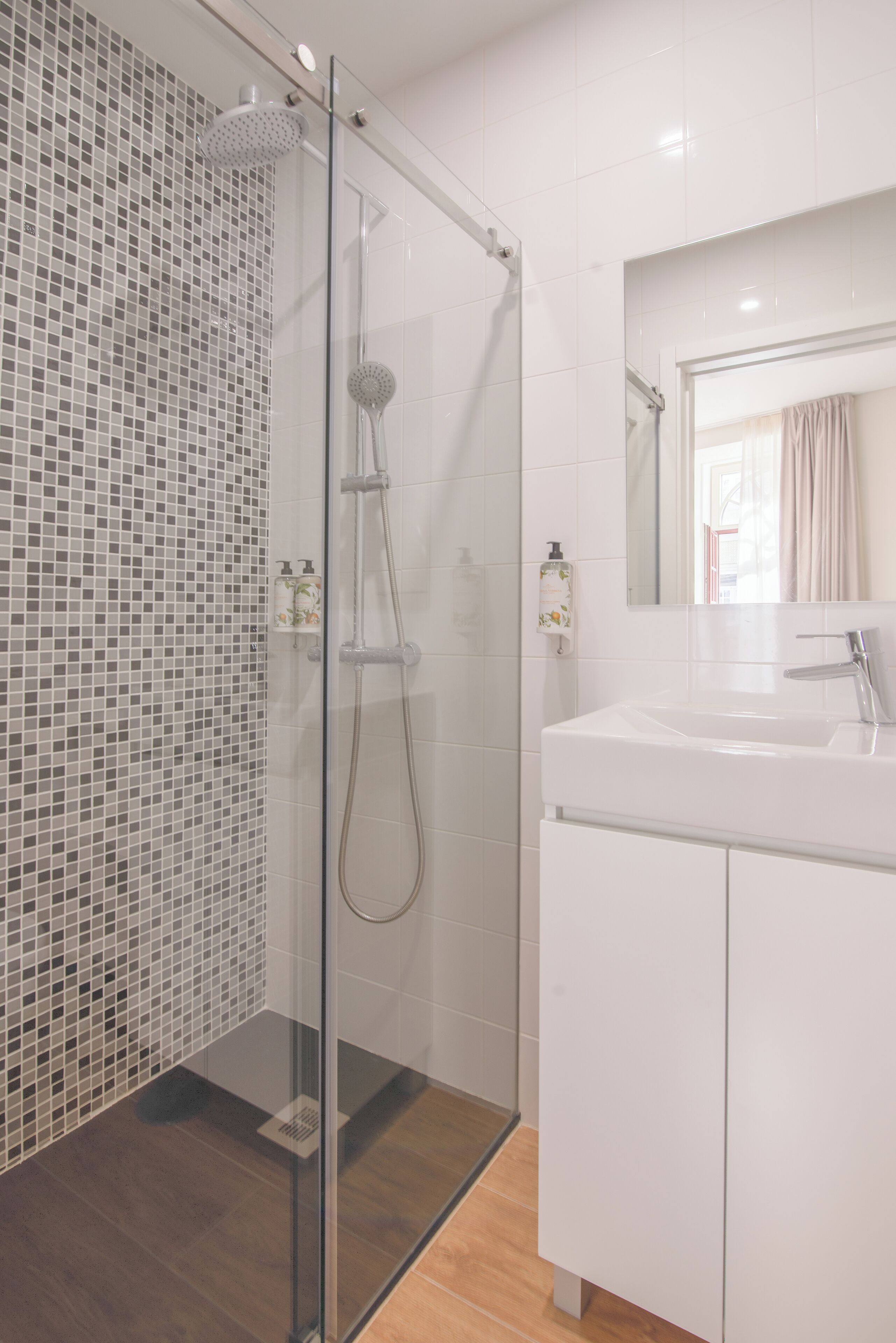 A modern bathroom with a glass shower enclosure, white tiled walls, and a white sink with a mirror above it.