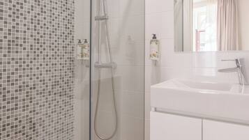 A modern bathroom with a glass shower enclosure, white tiled walls, and a white sink with a mirror above it.