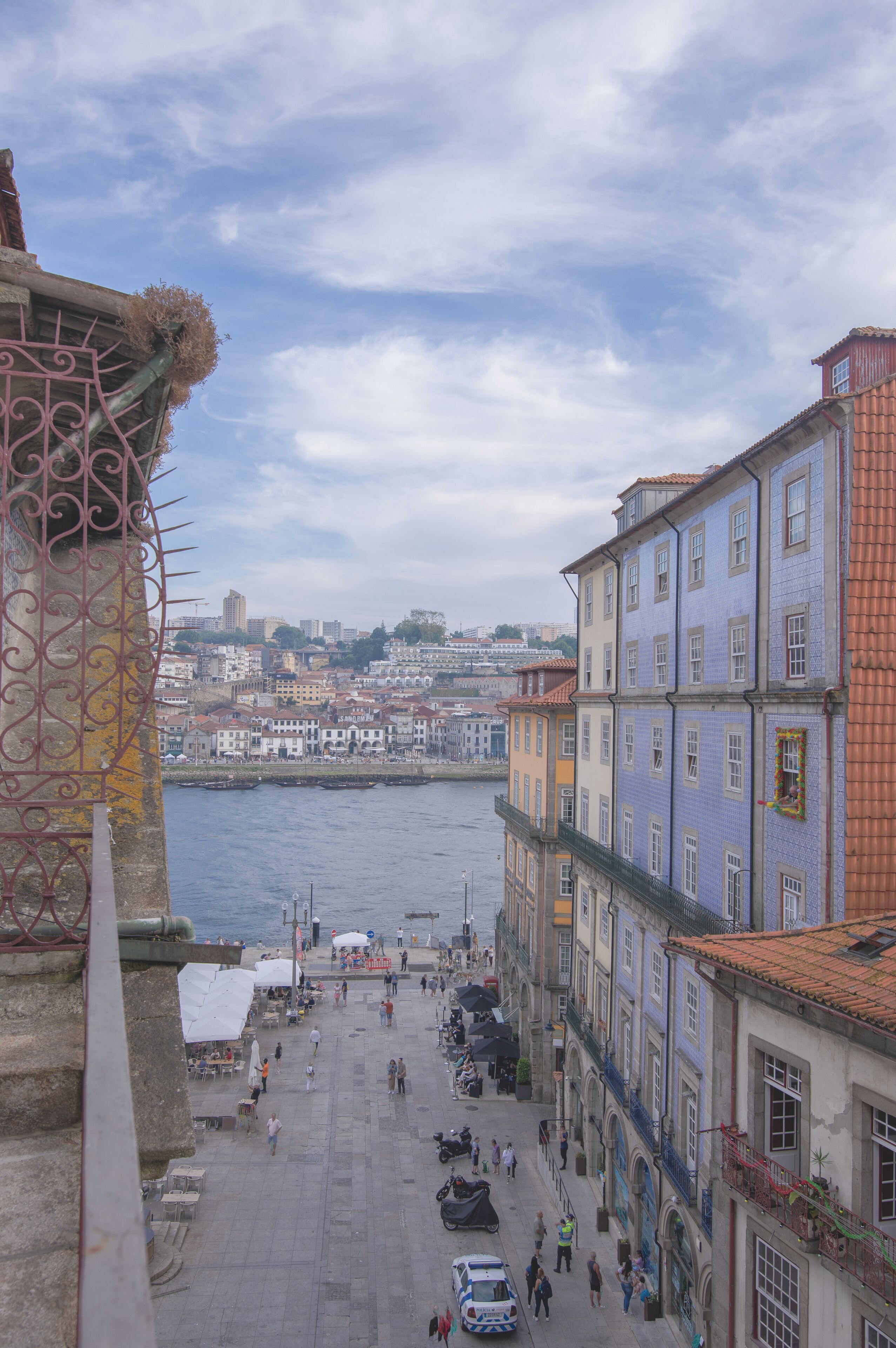 Uma rua à beira-rio, com edifícios, uma ponte e vista do horizonte urbano.
