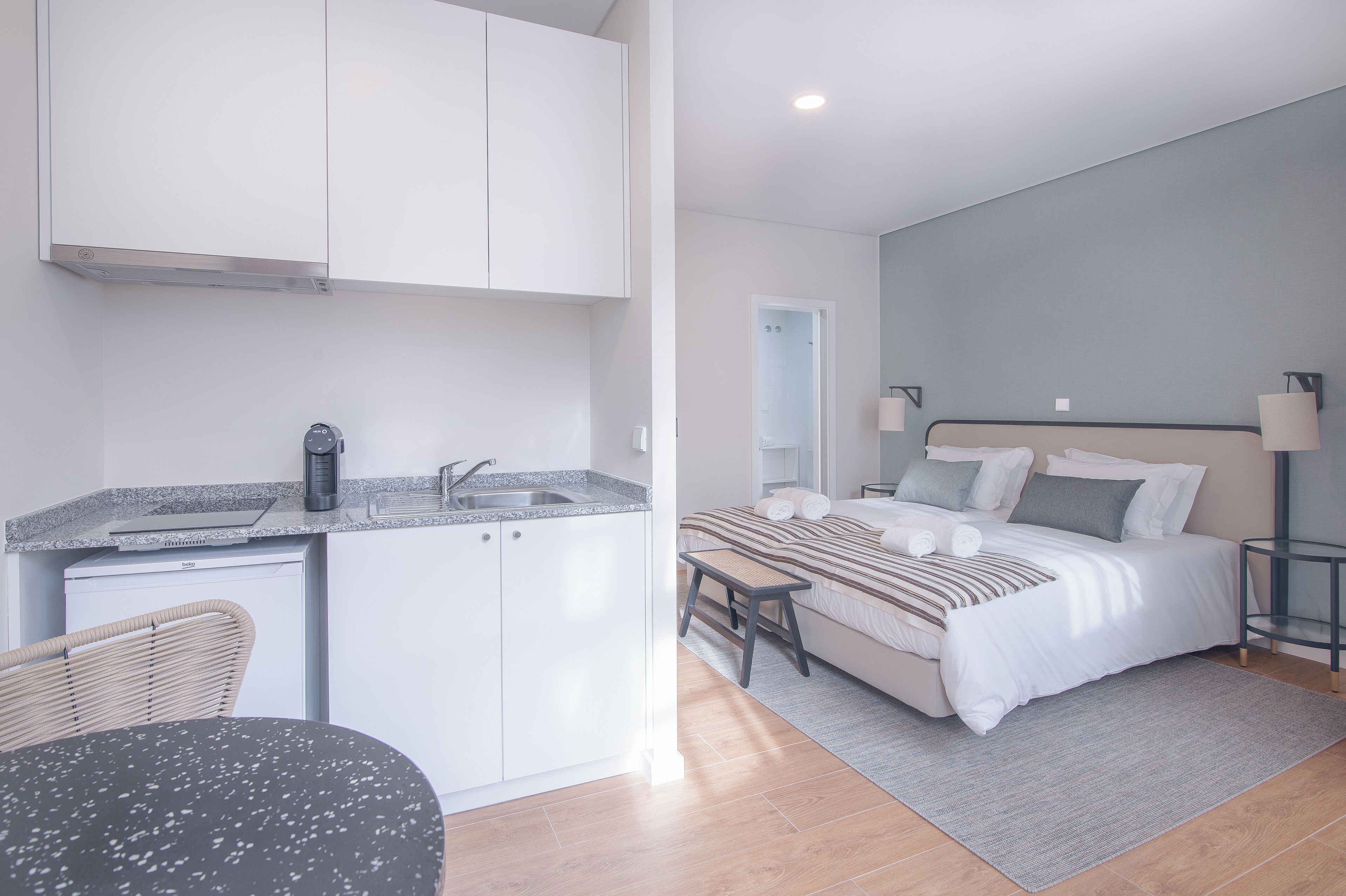 A compact room with a kitchenette, a bed, and a bedside table.