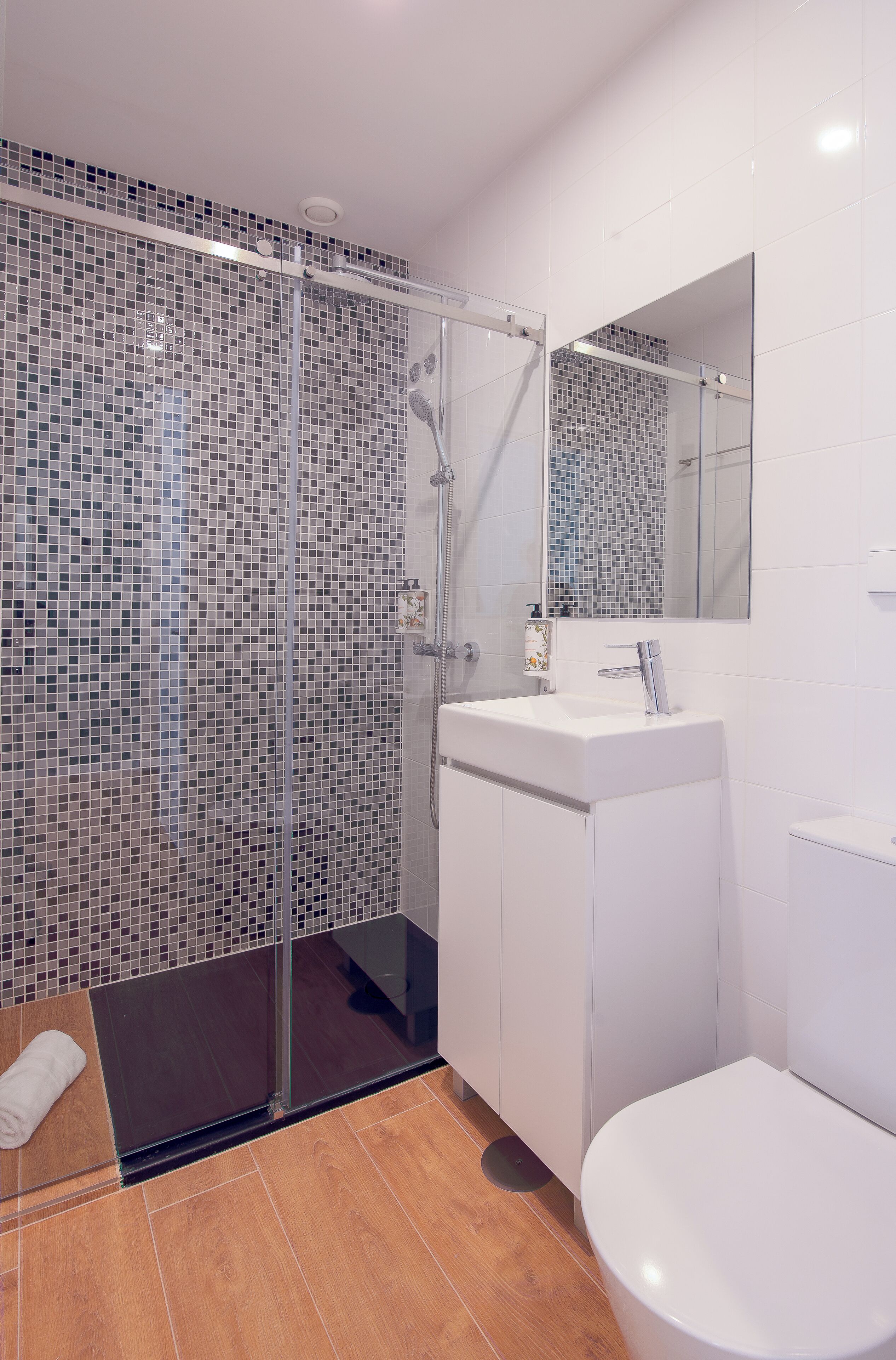 A modern bathroom with a glass shower enclosure, a white sink, and a toilet.