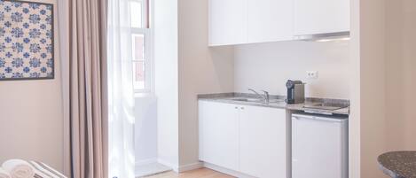 Uma cozinha compacta com armários brancos, forno embutido e um refrigerador pequeno.