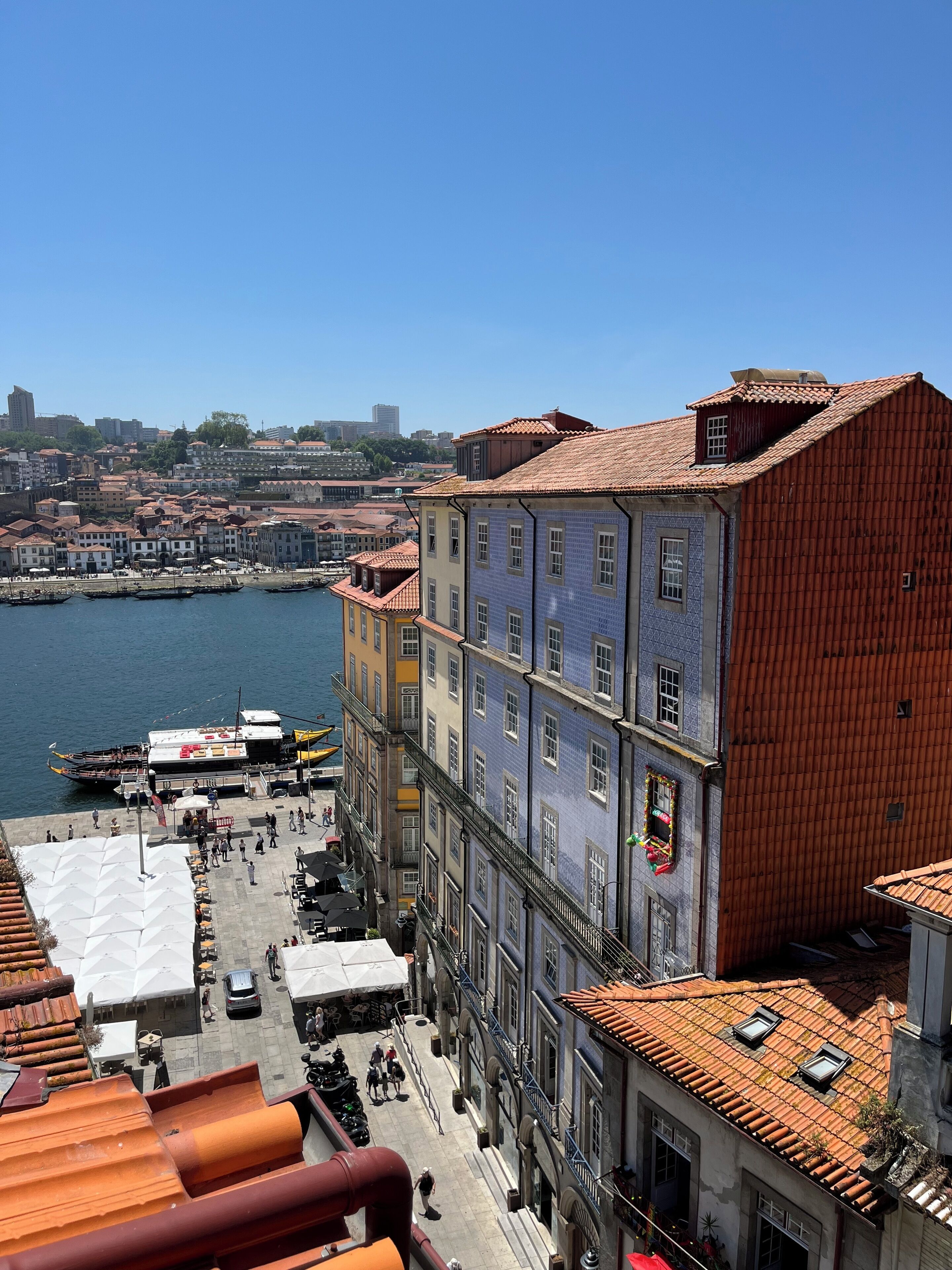 A waterfront promenade with buildings featuring traditional architecture, a clear sky, and a view of the cityscape in the background.
