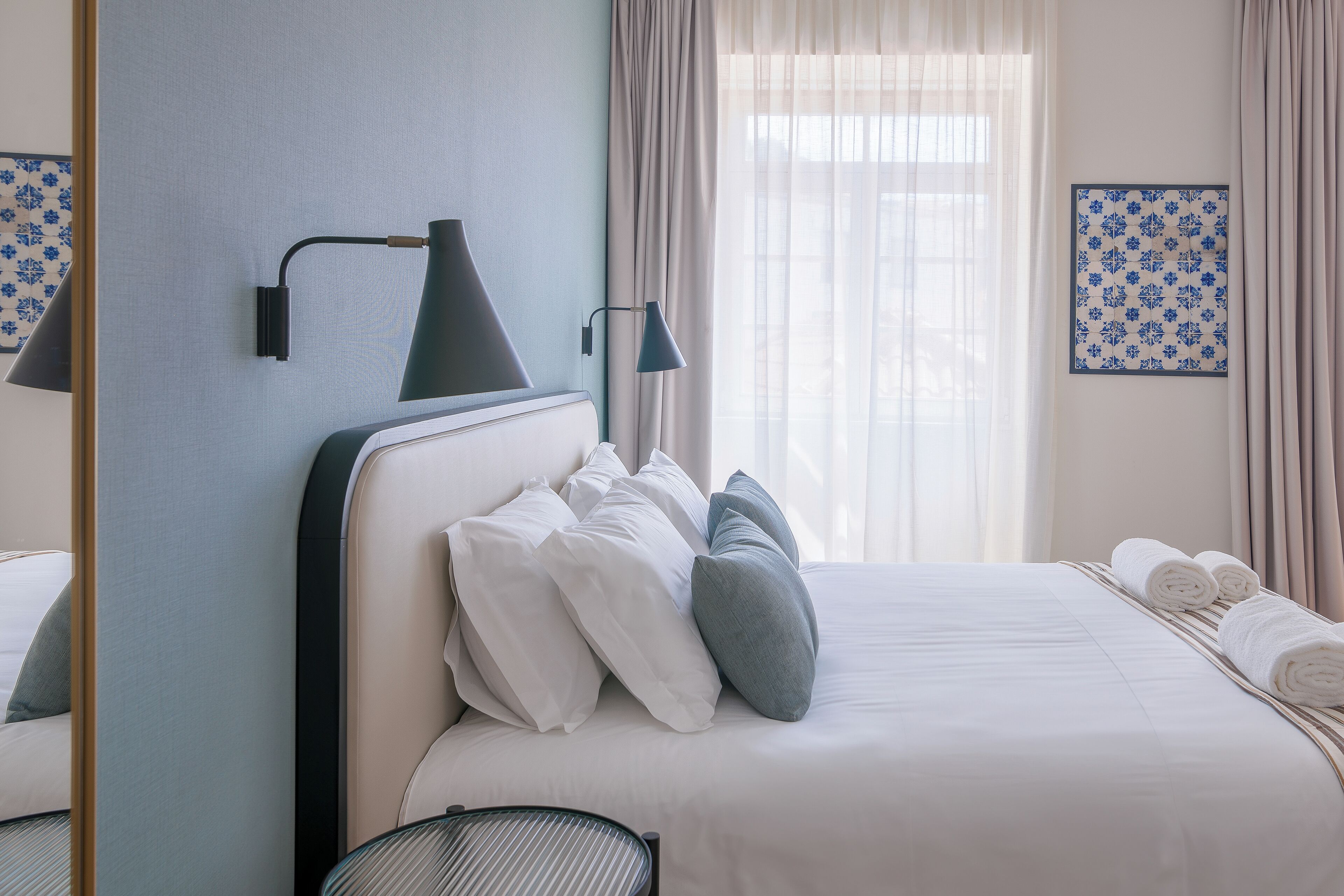 A neatly made bed with white and grey pillows, a bedside lamp, and a framed artwork on the wall.