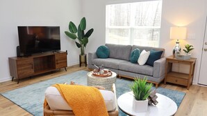 Un salon moderne avec un canapé gris, un meuble TV en bois, une table basse ronde et une grande plante.