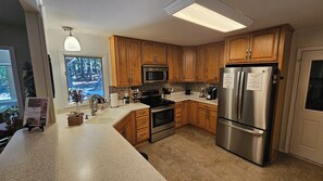A modern kitchen with wooden cabinets, stainless steel appliances, a large window, and a view of the outdoors. - The Village Getaway in HSV (Hot Springs Village)