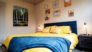 Une chambre à coucher avec un grand lit, une tête de lit, des tables de chevet et des œuvres d’art murales.