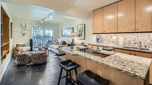 A modern kitchen with granite countertops, wooden cabinets, and a built-in island with stools. - Enjoy this Intimate 1-Bedroom Retreat in the Heart of Vail (Vail)