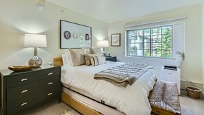 A bedroom with a bed, bedside tables, a window, and a wall-mounted air conditioner. - Enjoy this Intimate 1-Bedroom Retreat in the Heart of Vail (Vail)