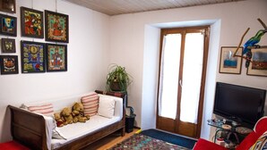 A cozy living room with a wooden sofa, a red armchair, a television, and various framed artworks on the wall. - Apartment in Vallemaggia Cevio (Cevio)