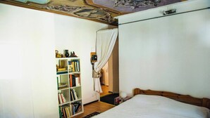 A bedroom with a wooden bed, a bookshelf with books, a curtain, and a ceiling with a decorative design. - Apartment in Vallemaggia Cevio (Cevio)