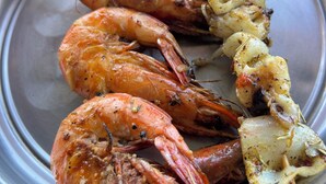 Un plato con camarones a la parrilla y verduras ensartadas.