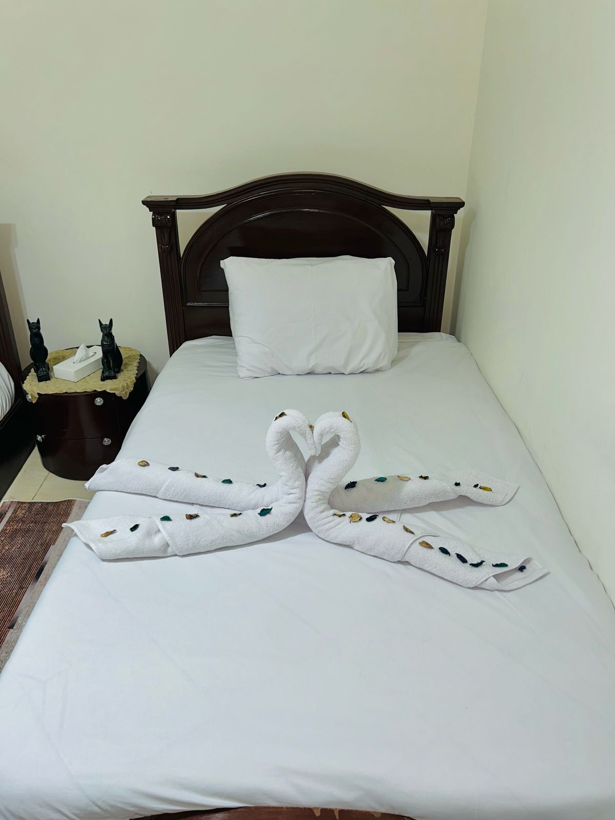 A neatly made bed with a white pillow and a towel arranged in a swan shape.