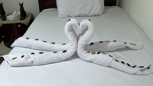 A neatly made bed with a heart-shaped towel arrangement, a white pillow, and a dark wooden headboard. - Bastet Pyramids View Inn (Giza)