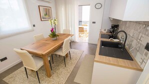 A modern kitchen with a wooden table and chairs, a sink, and a small balcony visible through the door. - Holiday apartment with air conditioning (Poreč)