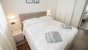 A bedroom with a large bed, two wall-mounted lights, a bedside table, a wardrobe, and two framed pictures on the wall. - Holiday apartment with air conditioning (Poreč)