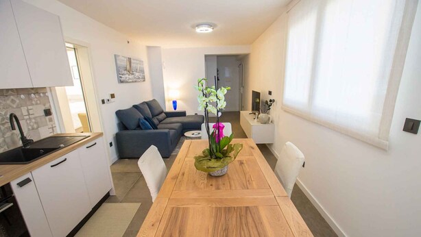 A modern kitchen with white cabinets, a wooden countertop, and a sink. There is a dining area with a wooden table and chairs, and a potted orchid on the table. - Holiday apartment with air conditioning (Poreč)