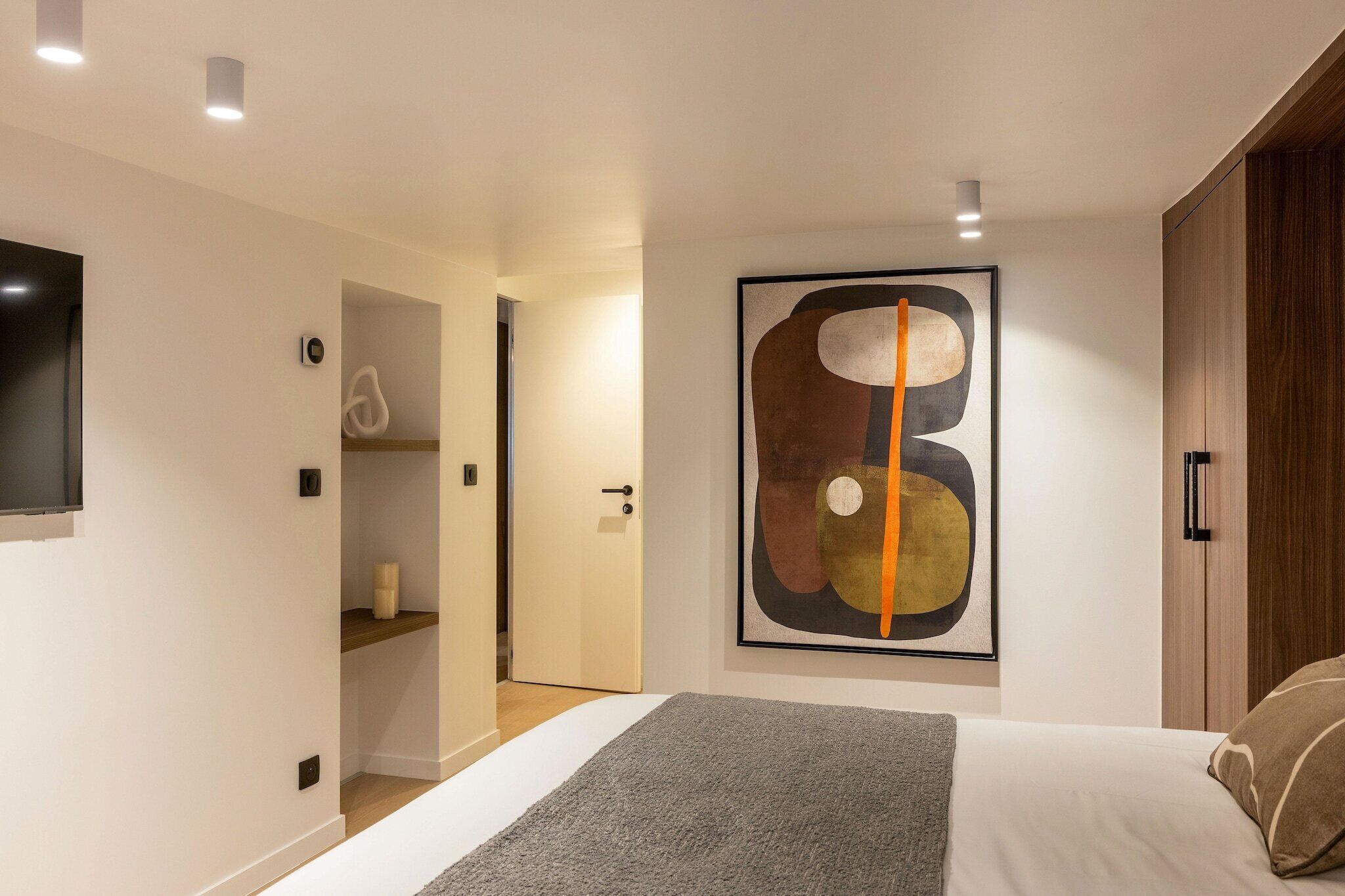 Un dormitorio moderno con un cuadro abstracto grande, un televisor de pantalla plana y un armario de madera.