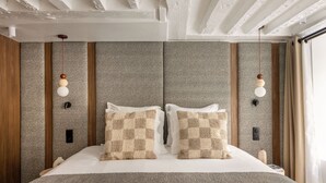 A modern hotel room with a large bed, checkered throw pillows, a wooden headboard, and a ceiling with exposed beams.