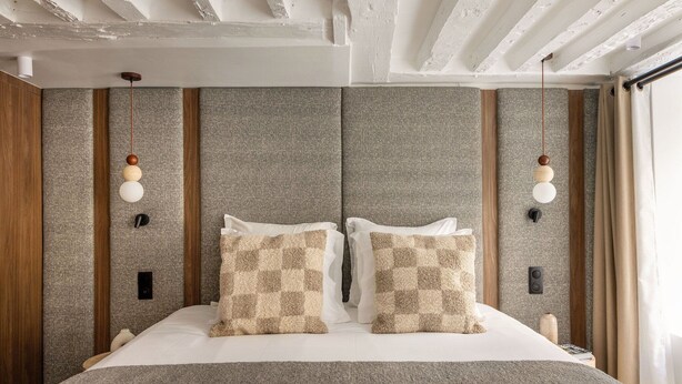 Een moderne hotelkamer met een groot bed, kussens met een ruitpatroon, een houten hoofdeinde en een plafond met zichtbare balken.
