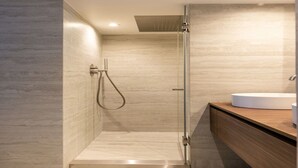 Een moderne badkamer met een glazen douchecabine, een houten wastafelmeubel en een betegelde muur van marmer.