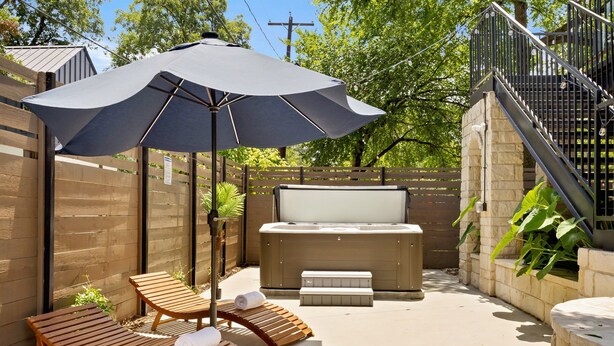 Un espace patio aménagé avec des fauteuils de jardin en bois, un grand parasol, un jacuzzi et un mur en pierre.