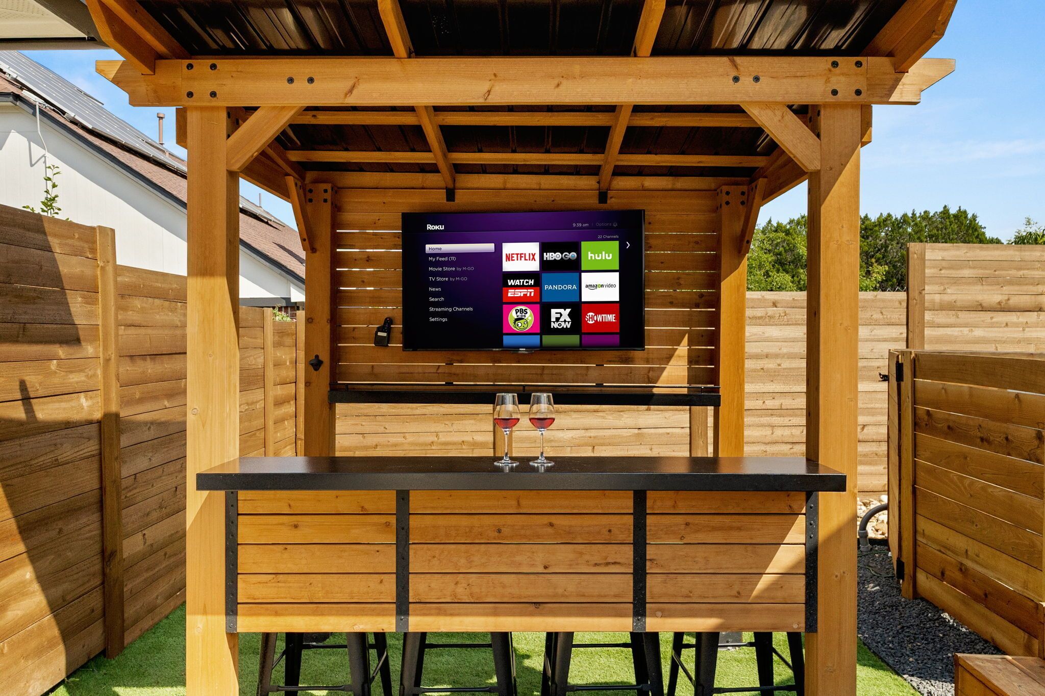 Una pérgola de madera al aire libre con un televisor que muestra varios canales de transmisión.