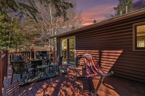 Una terraza de madera con mobiliario exterior, una hamaca y vistas a una zona boscosa.