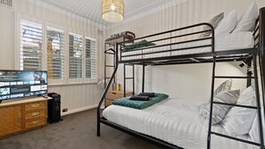A bunk bed room with a TV on a wooden dresser, a fan, and a window with blinds.