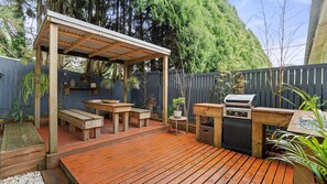 A wooden deck with a pergola, a barbecue grill, and outdoor seating.