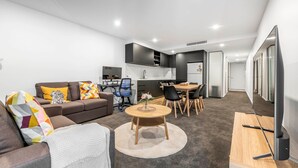 A modern apartment with a living room, dining area, kitchen, and a hallway leading to a bedroom.