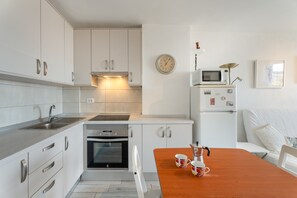Una cucina compatta con mobili bianchi, un forno a microonde, una sveglia e una macchina da caffè sul piano di lavoro.
