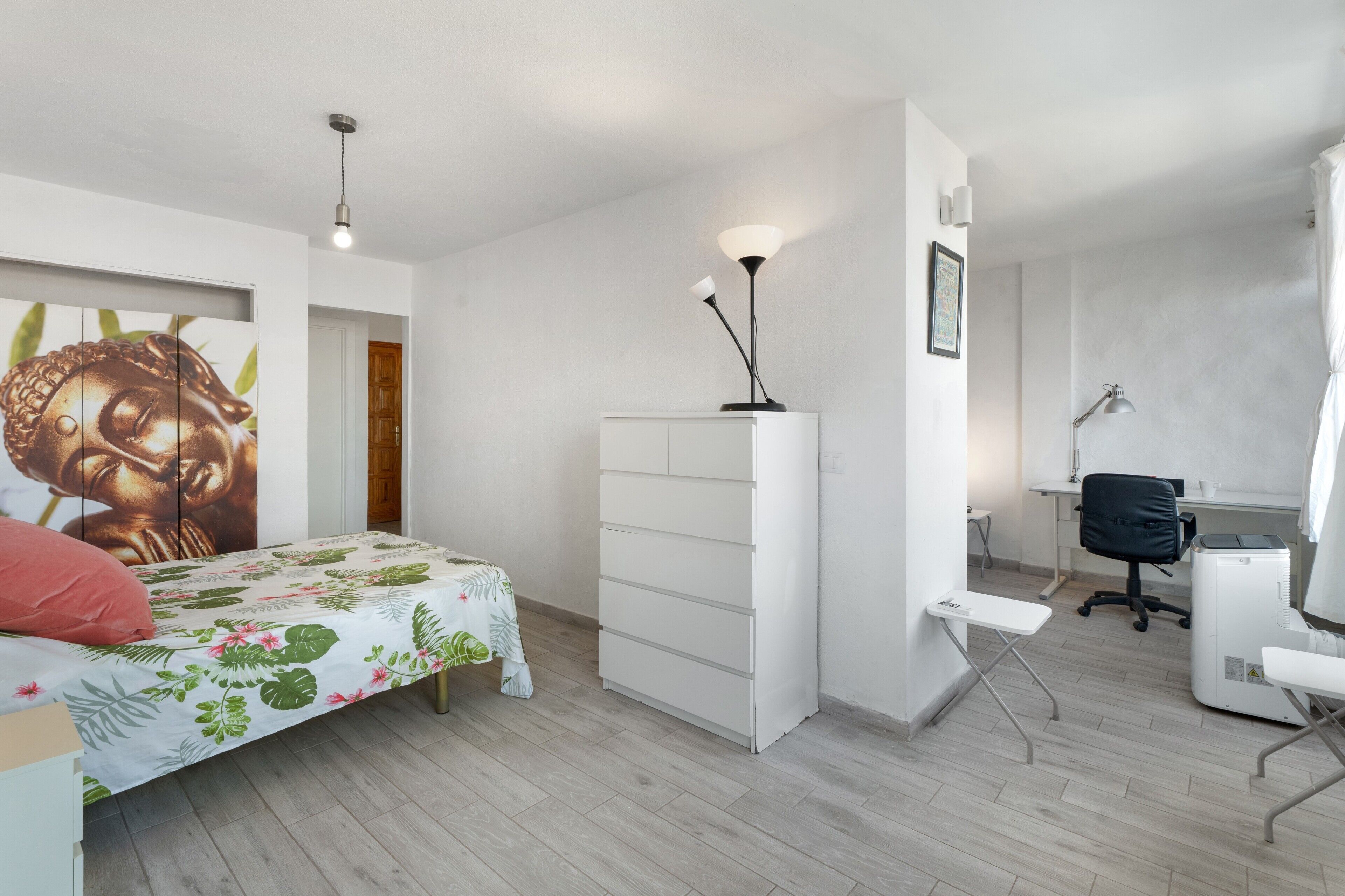 Une chambre à coucher comprenant un lit, un bureau, une chaise, une armoire et une grande statue de Bouddha.