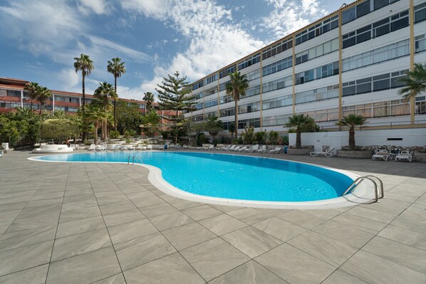 A swimming pool with a curved edge, surrounded by lounge chairs and palm trees.